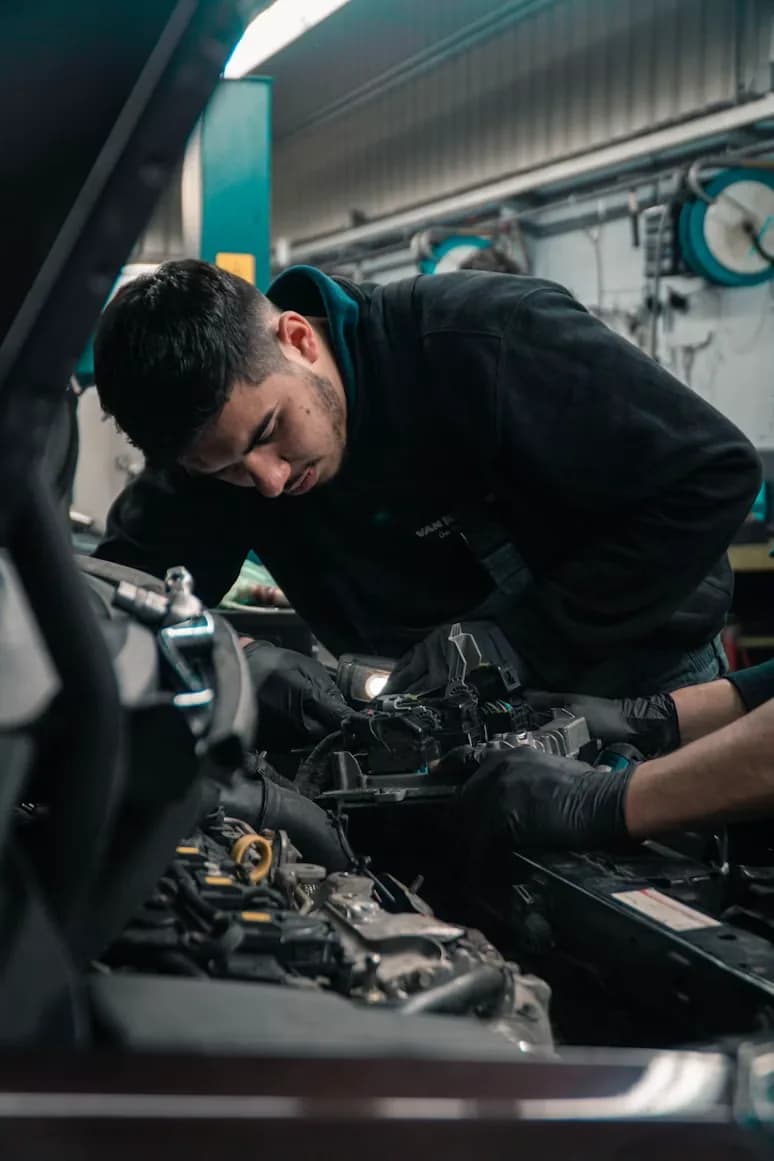 Technicien penché sur un moteur, capot ouvert, dans un atelier